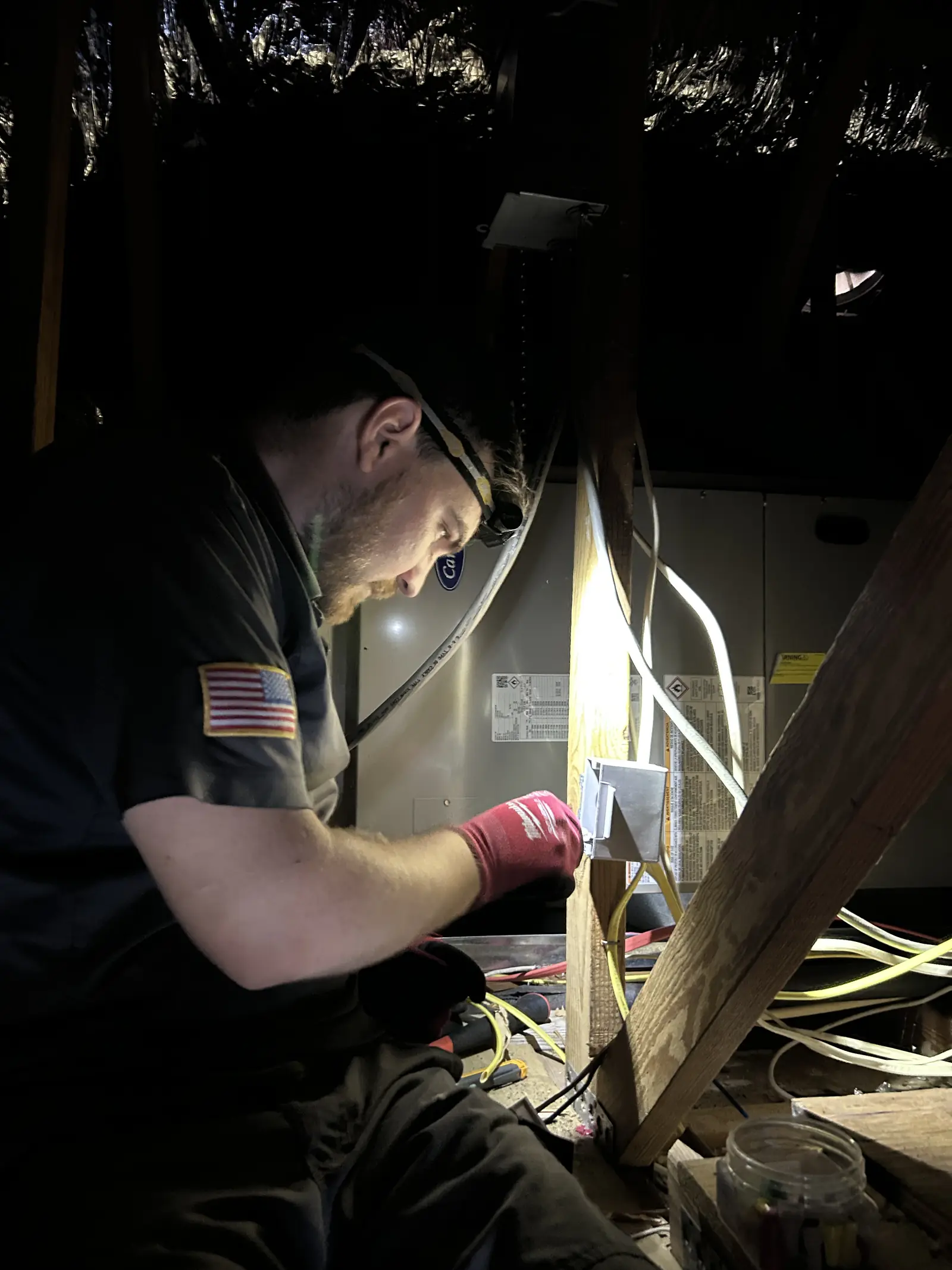 Kincaid Electric electrician with a headlamp wiring a circuit in a dark attic