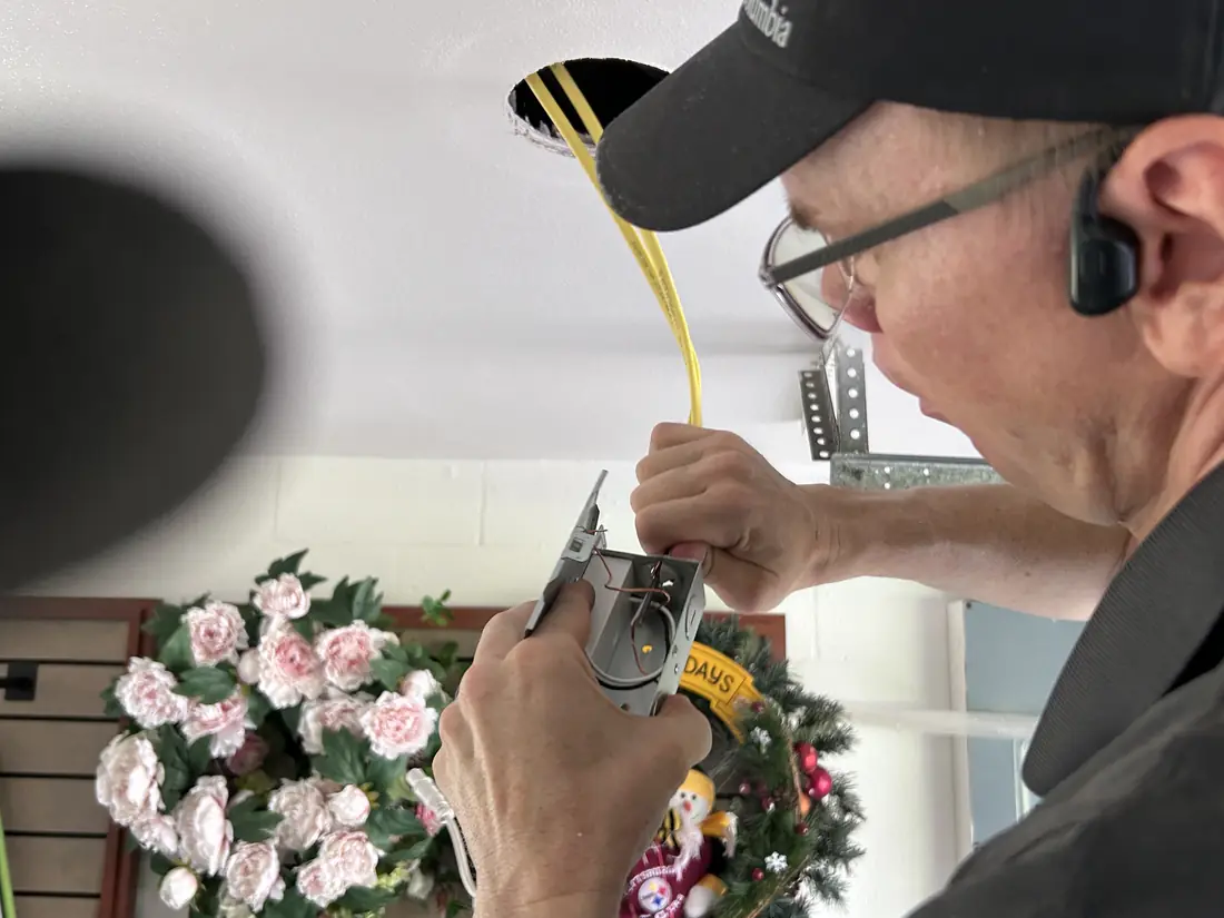 Kincaid Electric electrician wiring a ceiling light fixture next to a holiday wreath