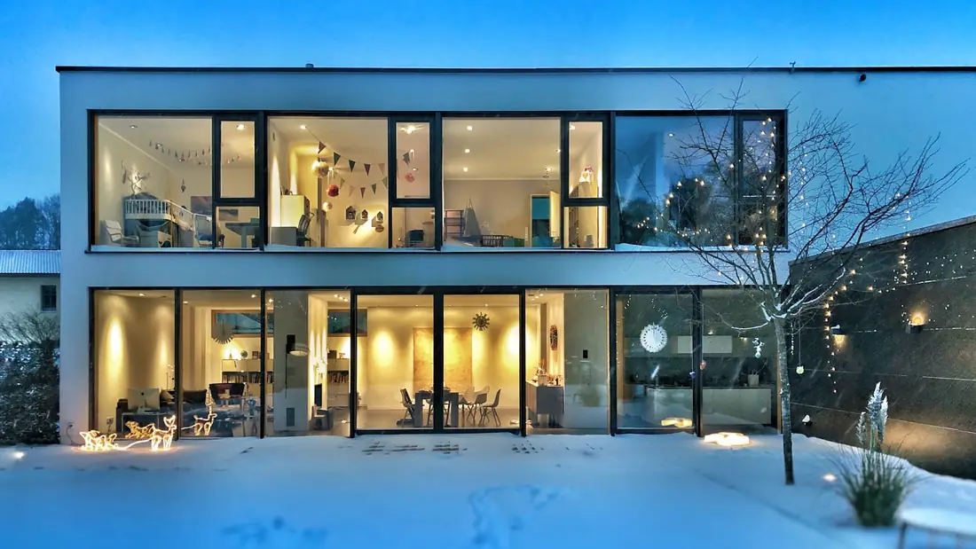 Modern glass fronted house lit up at dusk with smart home lighting